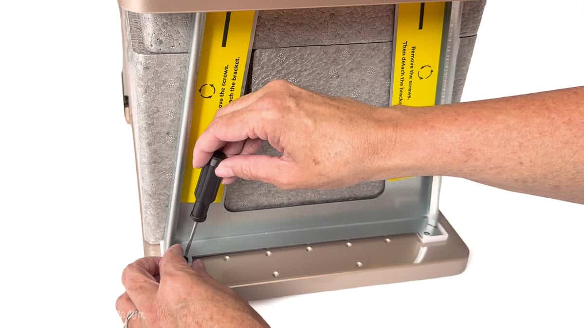 Hands using a screwdriver to remove shipping screws from the bottom of an xTool F2 Ultra laser cutter during setup.