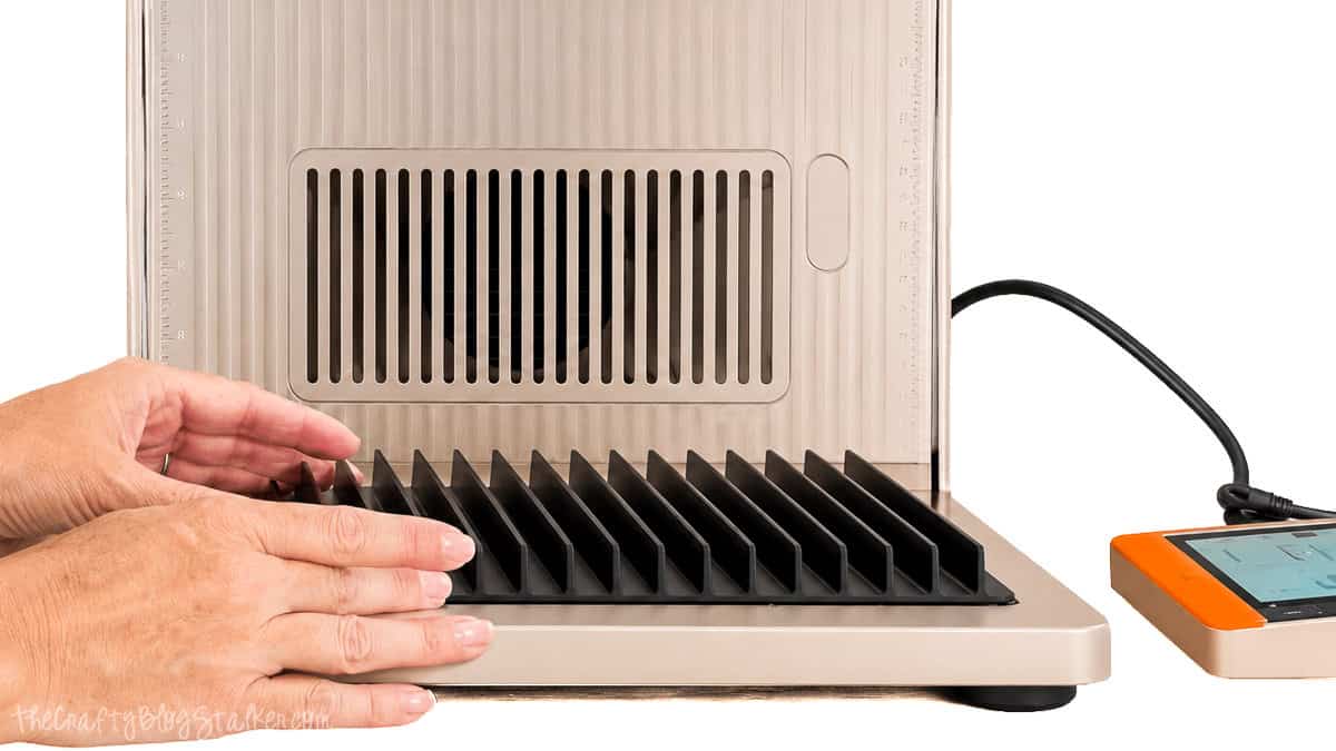Hands placing the slatted panel inside an xTool F2 Ultra laser cutter during setup, with the touchscreen controller visible beside the machine.