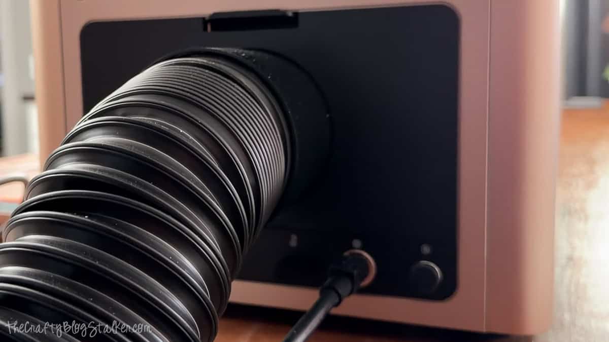 Rear view of an xTool F2 Ultra laser cutter with the exhaust vent hose securely connected for proper ventilation during use.