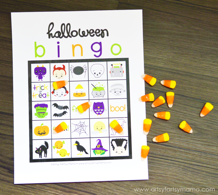 Printable Halloween bingo card with colorful spooky characters and candy corn pieces used as game markers on a dark wood table.