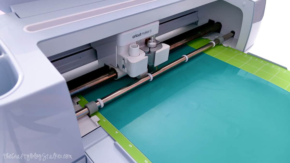 Cricut Maker 3 cutting teal puff vinyl on a green StandardGrip cutting mat.