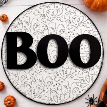 Halloween BOO door hanger with black letters and a ghost pattern, styled with orange pumpkins, a black spider, and plaid fabric.