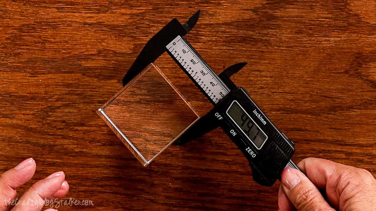 Digital calipers measuring the width of a rectangular crystal block on a wooden table before creating a 3D inner engraving.