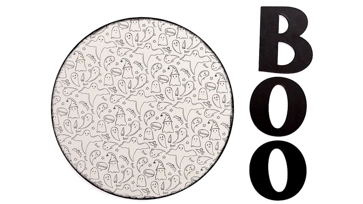 Round wooden Halloween sign with an engraved ghost pattern beside three black wooden BOO letters, ready for assembly.