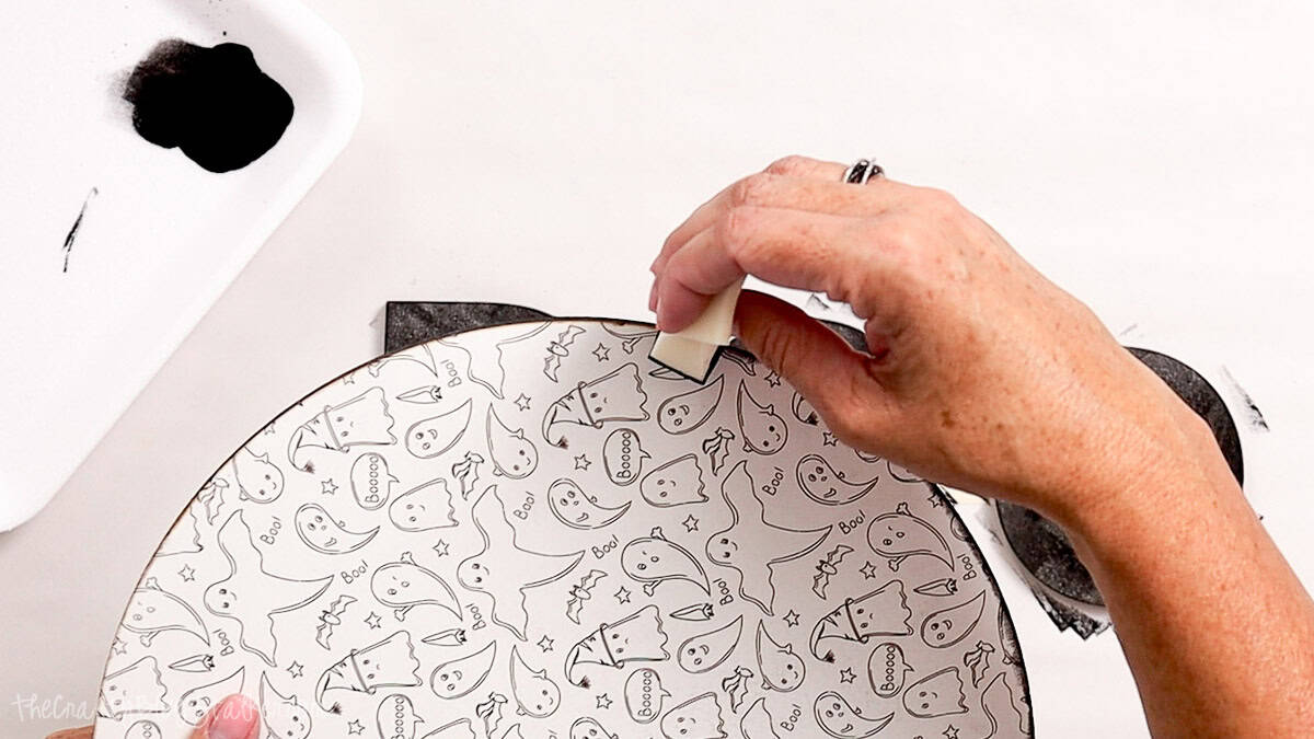 Hand painting the edge of a round ghost-patterned wooden Halloween sign black with a foam brush.