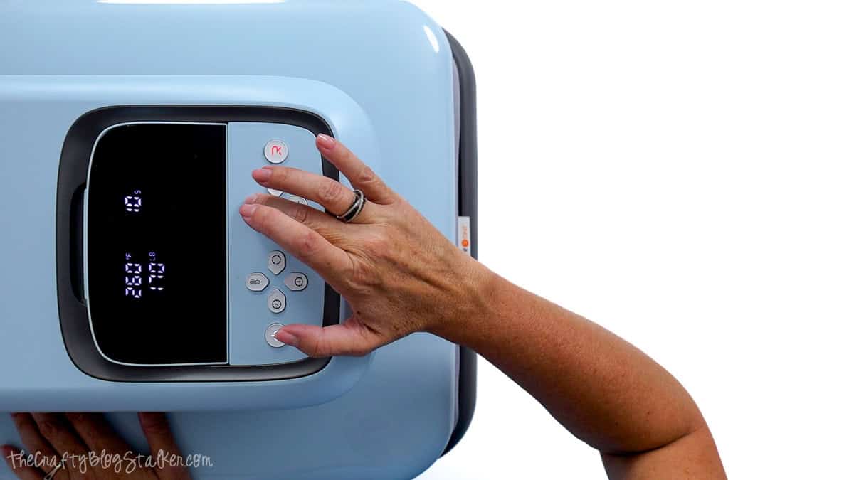Hand adjusting the temperature and time settings on a blue heat press before applying puff vinyl to a T-shirt.