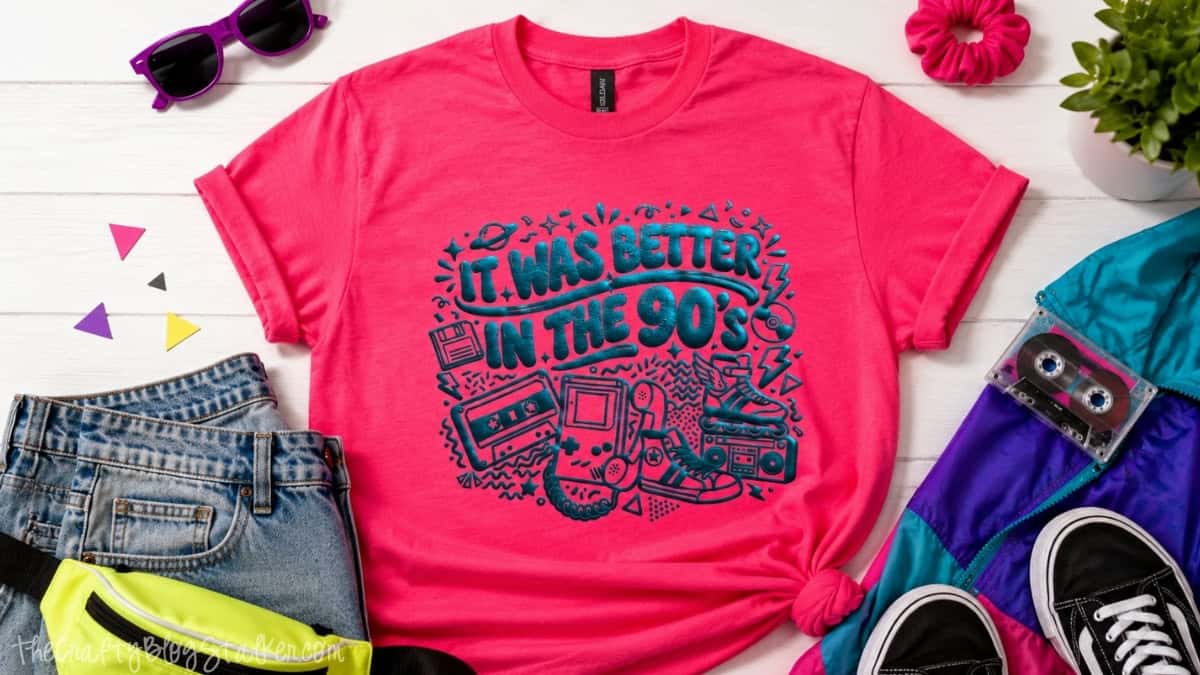 Pink T-shirt with raised blue puff vinyl reading It Was Better in the 90's, styled with retro clothing, a cassette tape, and sneakers.