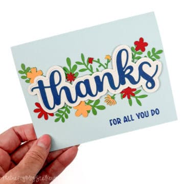 Light blue handmade thank you card with layered “thanks” lettering, colorful flowers and greenery, and “For All You Do” text.