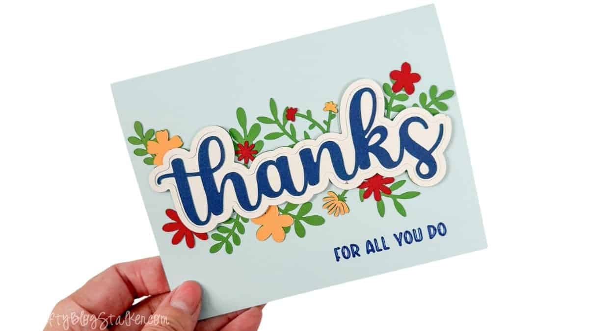 Hand holding a finished Cricut thank you card with layered blue