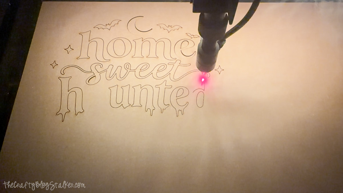 Laser cutting the Home Sweet Haunted Home Halloween sign design from a sheet of wood with bats, moon, stars, and lettering.