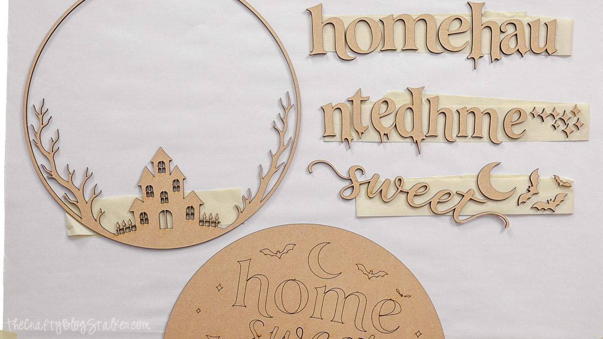 Laser-cut wood pieces for a Home Sweet Haunted Home sign, including a haunted house frame, spooky lettering, bats, moon, and engraved wood circle.