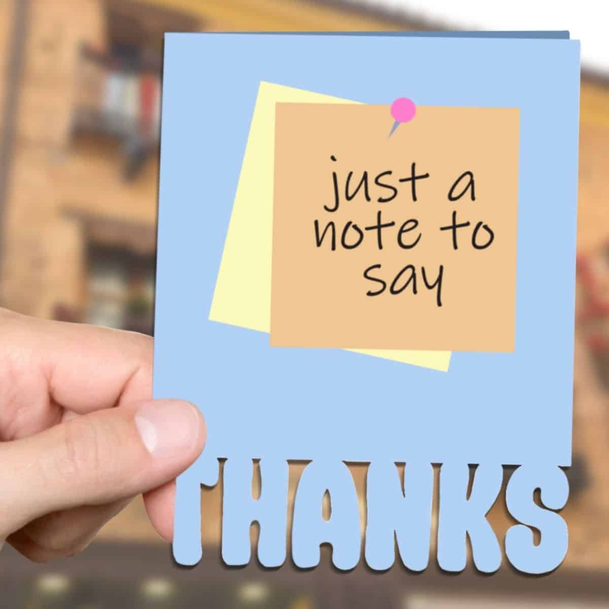 Blue thank you card held in a hand, featuring a pinned note that says
