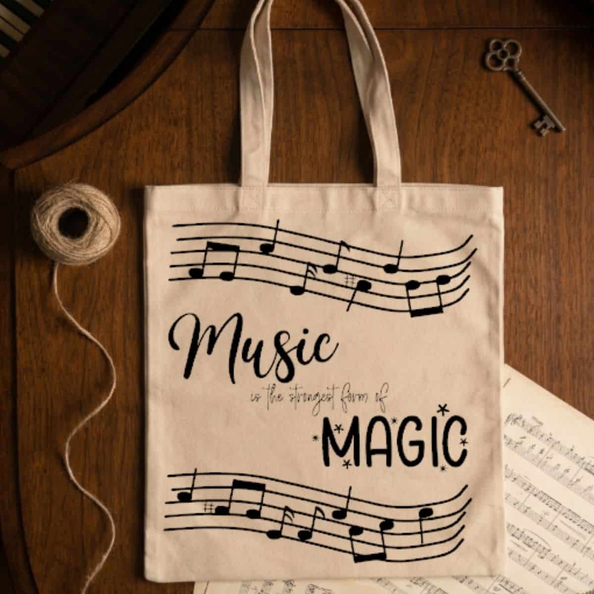 Beige canvas tote bag with the phrase "Music is the strongest form of magic" and black musical notes, displayed on a wooden table.