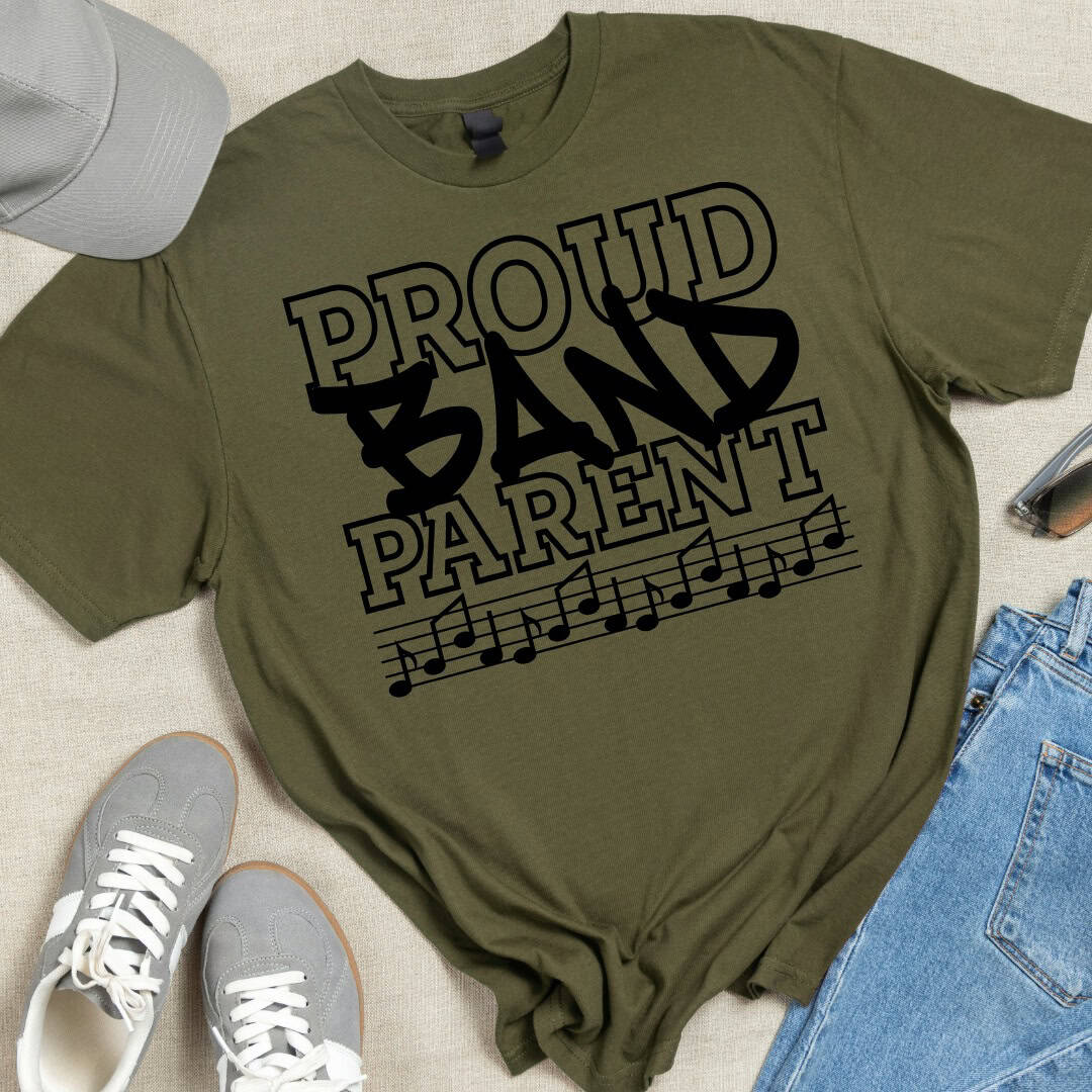 Olive green Proud Band Parent T-shirt with black lettering and musical notes, styled with blue jeans, gray sneakers, and a matching cap.