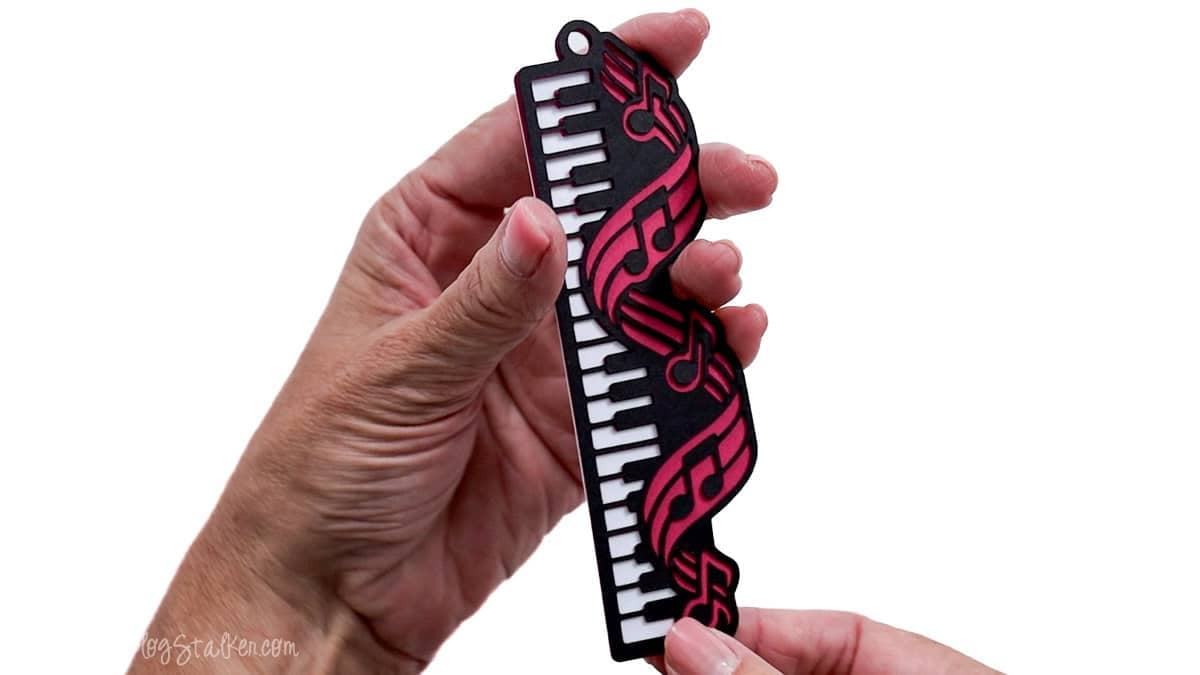 Hands holding a layered piano bookmark with black and white keys and pink musical notes while aligning the cardstock edges.