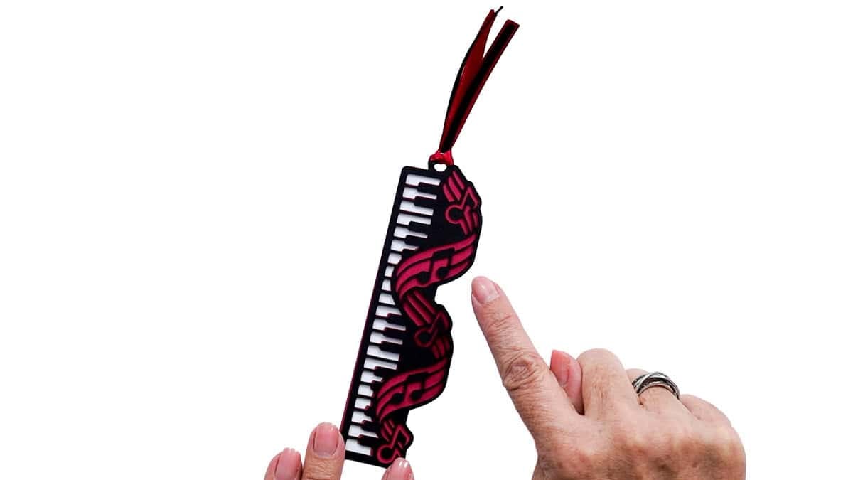 Finished layered piano bookmark with black and white keys, pink musical notes, and a red and black ribbon tassel.