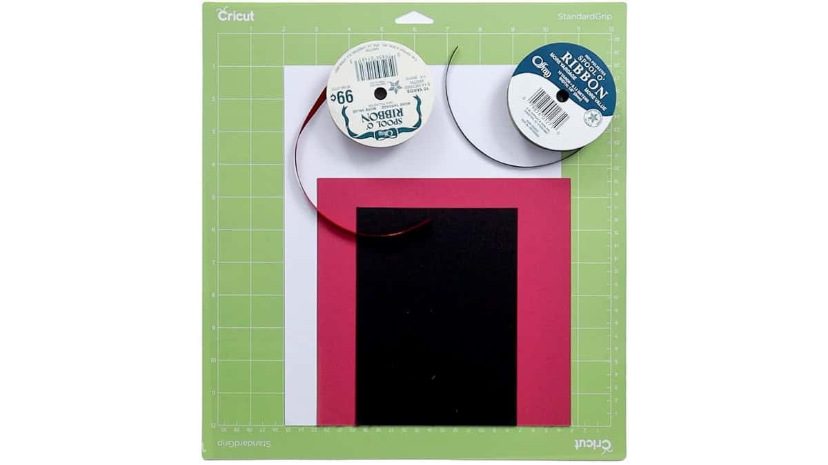 Cricut StandardGrip cutting mat with black, pink, and white cardstock and two spools of ribbon for making layered piano bookmarks.