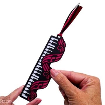 Hand holding a layered music bookmark with black piano keys, pink musical notes, and a coordinating ribbon tassel.