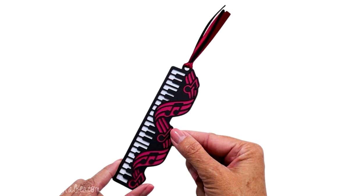 Hand holding a layered music bookmark with black piano keys, pink musical notes, and a coordinating ribbon tassel.