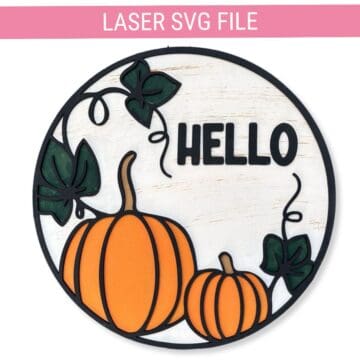 Round fall door hanger with two orange pumpkins, green leaves, and black text that says "HELLO," designed as a laser SVG cut file for seasonal decor.