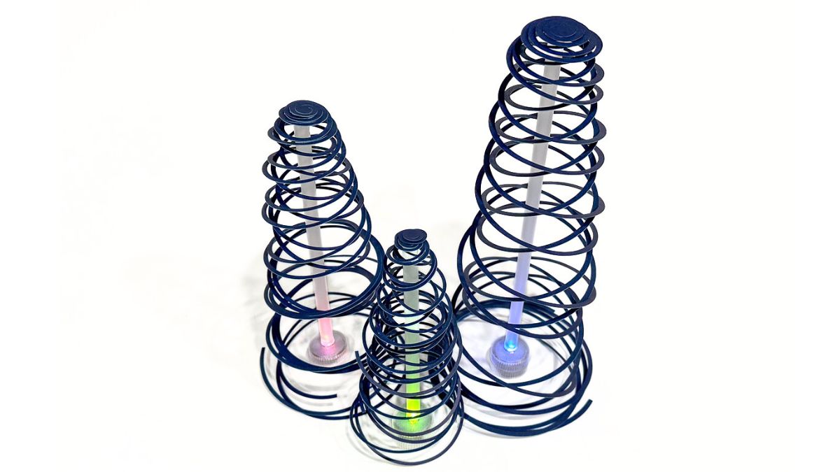 Three spiral cone trees made from coiled strips, each standing over a small LED light that glows in different colors.