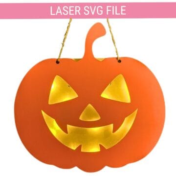 Orange jack-o'-lantern door hanger with glowing cut-out eyes, nose, and mouth, hanging from a string, made for Halloween decor.
