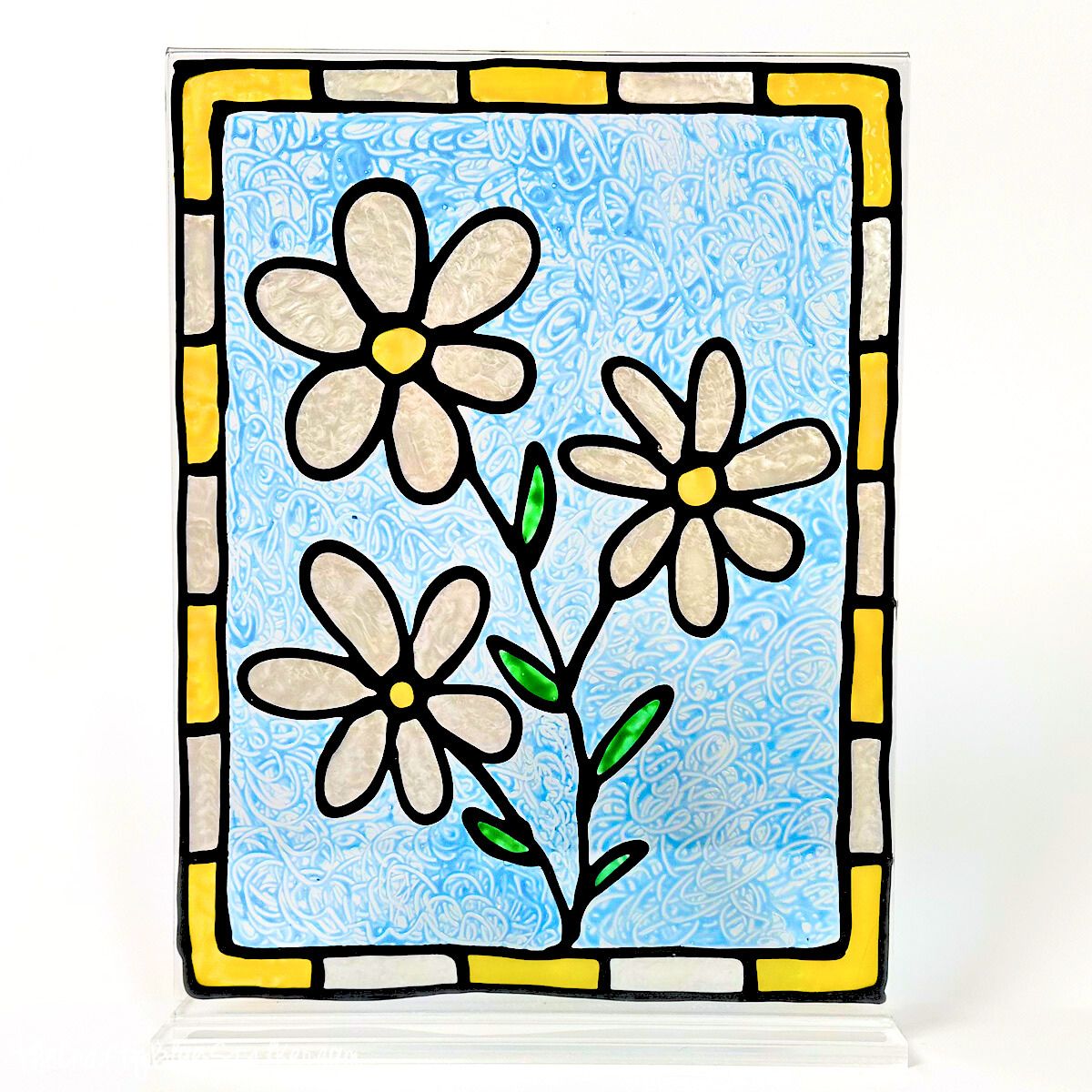 Faux stained glass panel with three white daisies, green stems, and a blue textured background, framed by a yellow and gray block border.