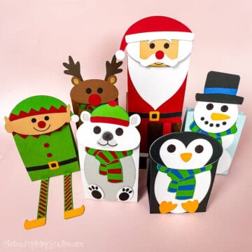 A group of holiday-themed gift bags shaped like Santa, a reindeer, an elf, a polar bear, a penguin, and a snowman, all decorated with bright colors and scarves.