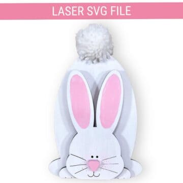 White wooden bunny decor with pink ears, a painted face, and a fluffy pom-pom tail, labeled as a laser SVG file for Easter crafting projects.