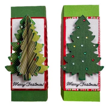 Two handmade Christmas gift boxes decorated with layered green paper trees, colorful gems, and “Merry Christmas” labels on red and green cardstock.