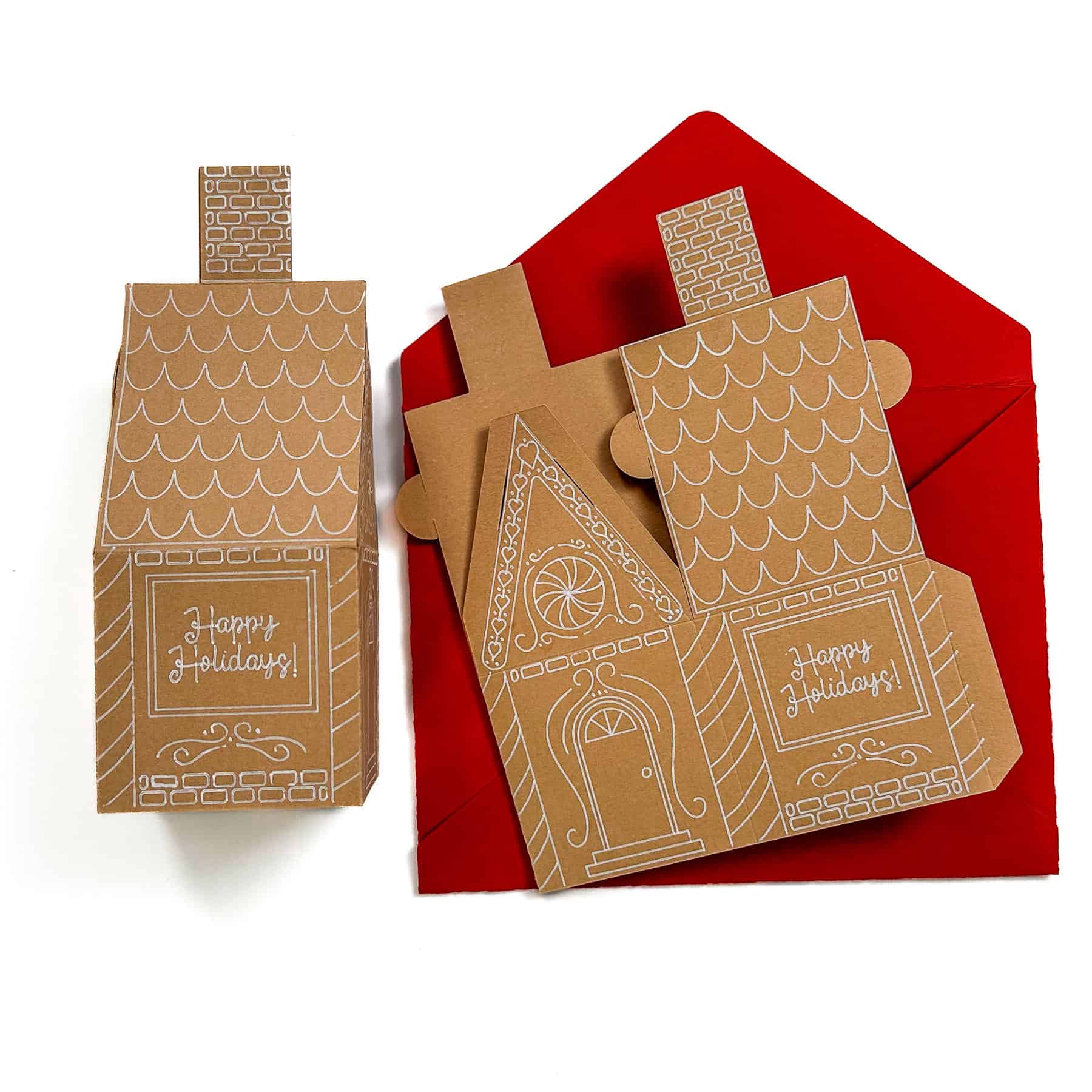 Handmade gingerbread house–shaped holiday cards with white designs and red envelopes, featuring “Happy Holidays” text.