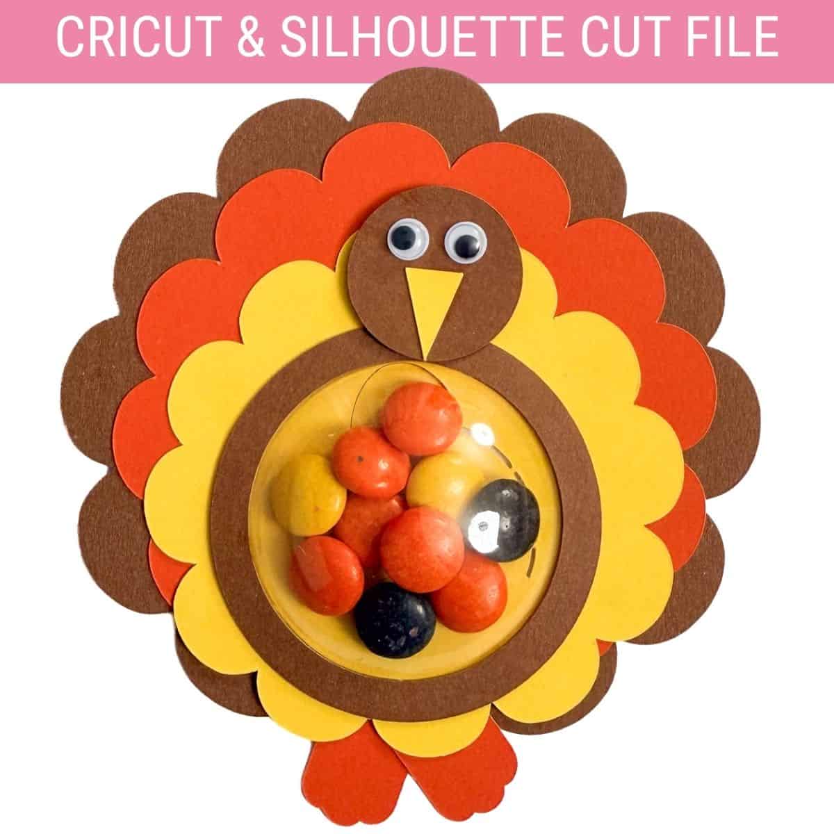 Paper turkey candy holder made with a Cricut cut file, featuring layered feathers, googly eyes, and a clear dome filled with colorful candy.